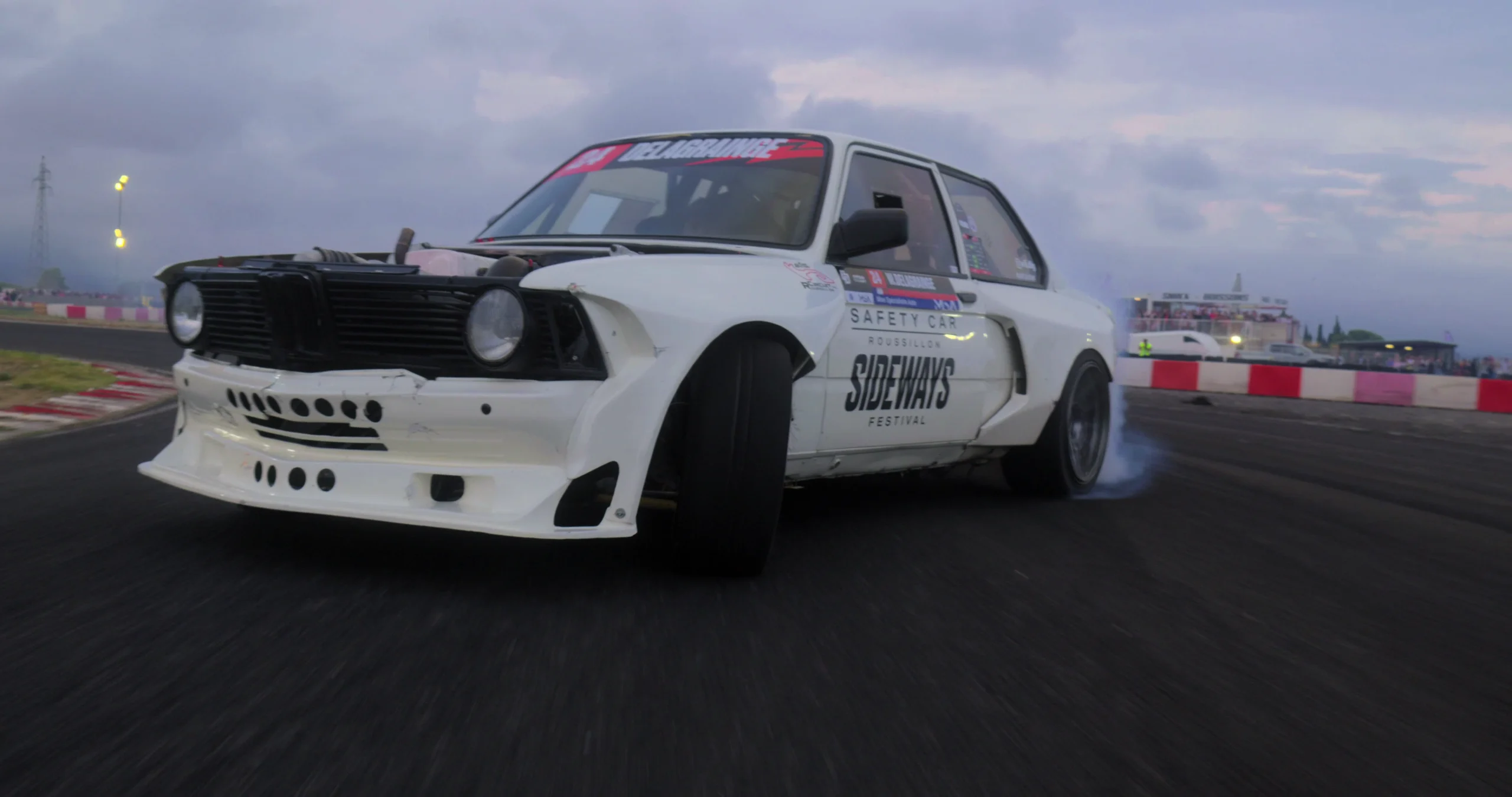 La BMW E21 blanche de Wilson Delagrainge en pleine glisse sur un circuit, fumée aux roues arrière.